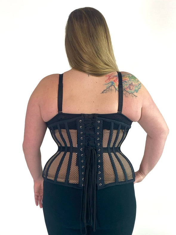 back lace up view of a plus size curvy model wearing the 426 longline mesh waist training black corset with a black bra and black leggings