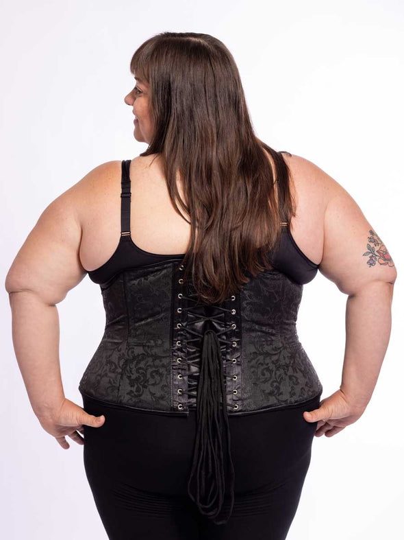 curvy plus size model wearing a black bra and leggings and a black brocade corset back lace up view