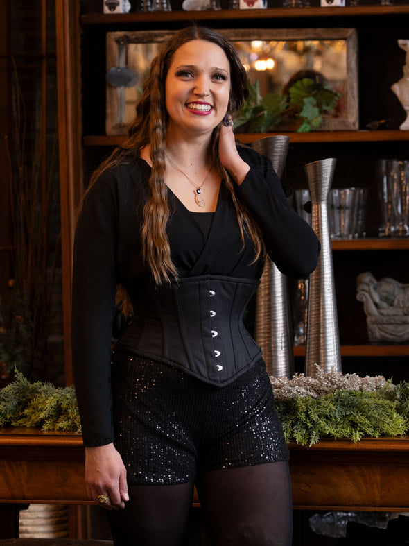 Woman wearing a 201 waspie black corset and sparkly shorts in a decorative setting.