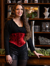 woman with long hair standing in a lounge wearing a red velvet coset for waist training and fashion with sequin shorts and over the knee 