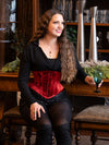 woman with long hair sitting in a lounge wearing a red velvet coset for waist training and fashion with sequin shorts and over the knee boots