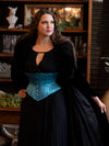 Woman wearing a black dress with a teal blue waspie corset belt in a room with decorative items.
