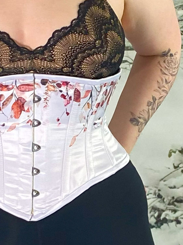 Close up detail view of a Model in a winter scene with hourglass waspie corset in winter white with a print over black lingerie with stockings