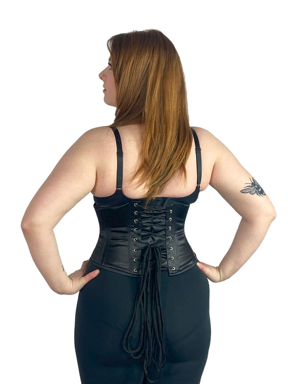 Smiling model wearing the cs220 waist training corset over leggings and a bra back lace up view