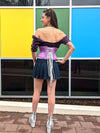 Back lace up corset view of Sassy cute model wearing a short lilac corset belt with front zipper closure. Standing with one hand on her hip and wearing a short denim skirt and platform shoes