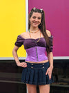 Sassy cute model wearing a short lilac corset belt with front zipper closure. Standing with one hand on her hip and wearing a short denim skirt and platform shoes
