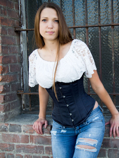 model wearing a 345 longline corset with ripped jeans and a lace top sitting on the windowsill of an abandoned warehouse