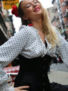 Woman in polka dot blouse with red flower in hair, outdoors with blurred background