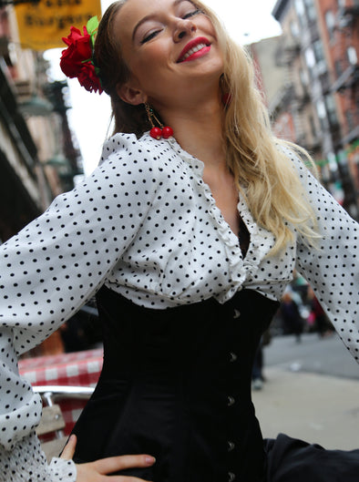 Woman in polka dot blouse with red flower in hair, outdoors with blurred background