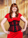 Red headed model wearing a red dress with a mesh waist training corset standing in a ballroon