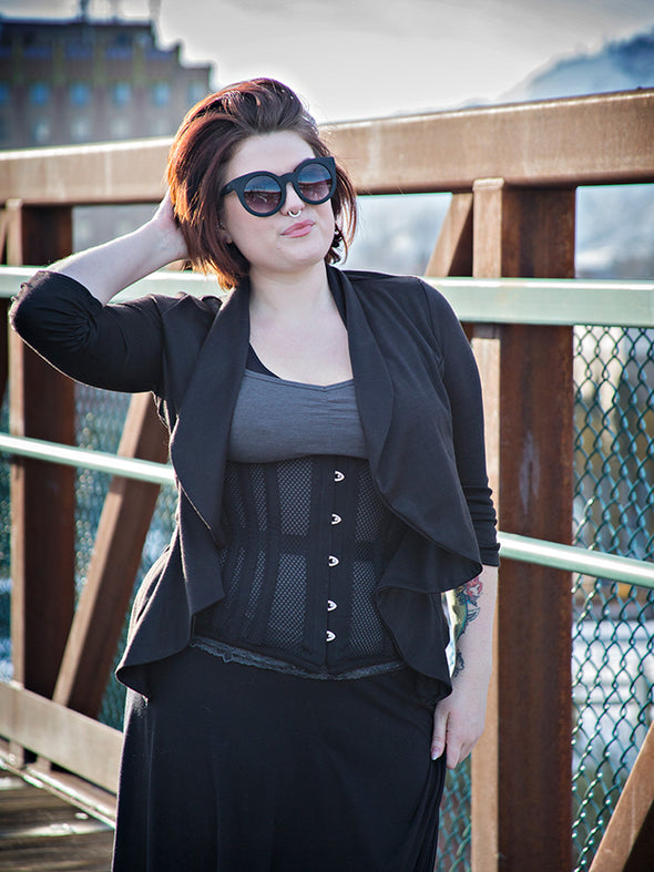 Woman wearing a cs426 hourglass curve black corset and black outfit with sunglasses on a bridge