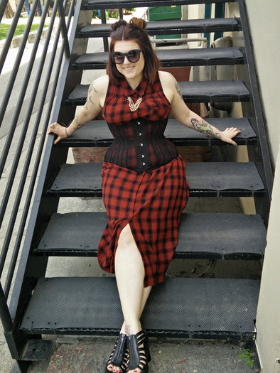 Woman in a red and black checkered dress sitting on a set of stairs wearing a black corset
