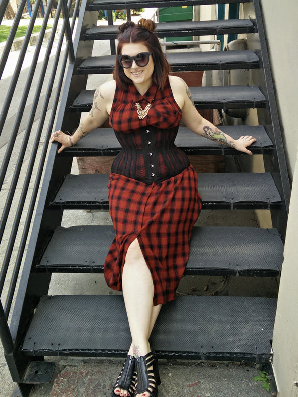 Woman in a red and black checkered dress sitting on a set of stairs wearing a black corset
