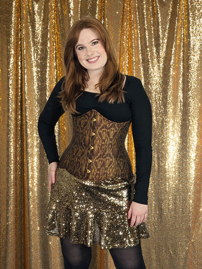 Auburn haired model wearing a black sweater and gold sequin skirt with a maroon and gold brocade corset