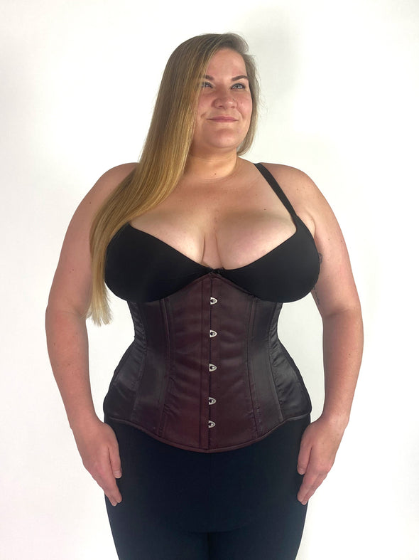 cute curvy plus size corset model wearing a shimmering maroon corset over a black bra and leggings