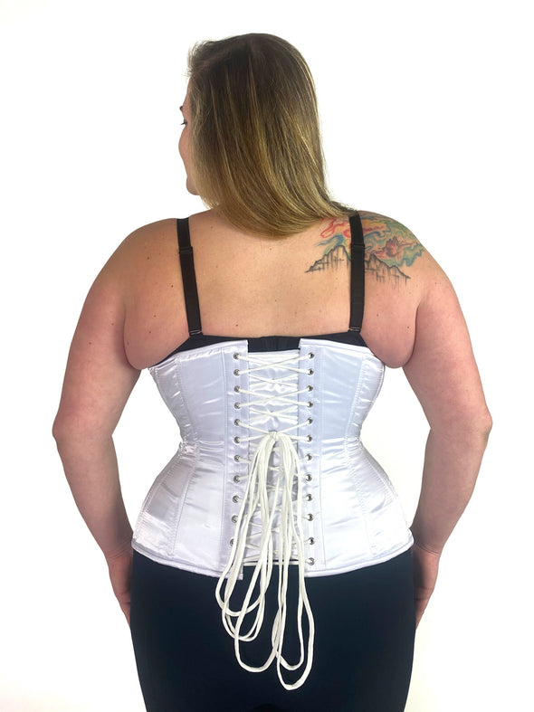 cute curvy corset model wearing a white satin corset over black leggings and black bra great for everyday wear fashion or waist training back lace up corset view