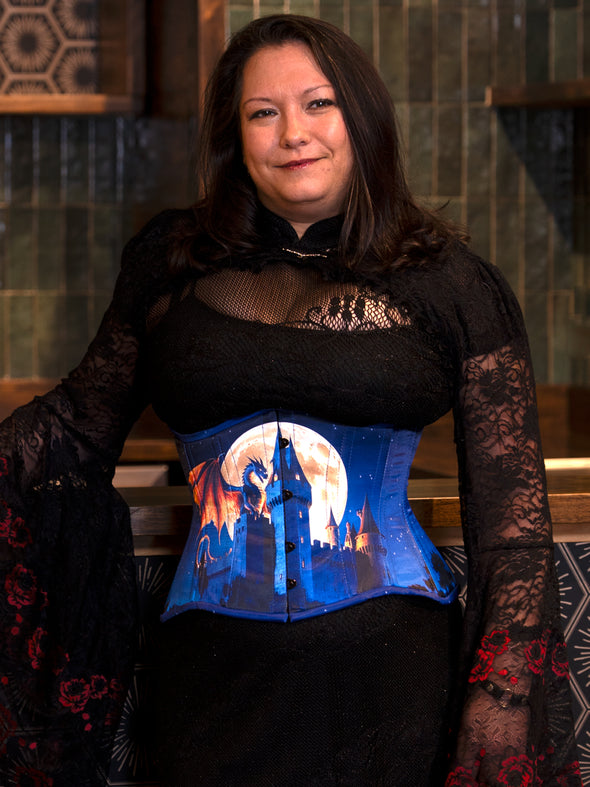 Person wearing a black lace top with a Halloween blue 426 hourglass curve corset featuring a castle  dragon design.