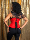 Back laceup corset view of Model with dark curly hair wearing a festive Holiday red corset with a sheer top and black pants