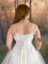 Back lace up corset view of a Model standing in a fantasy forest in a white fairycore dress with a white corset cs-426 Hourglass corset