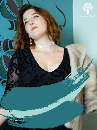 Woman wearing a black top and beige cardigan with a decorative blue background