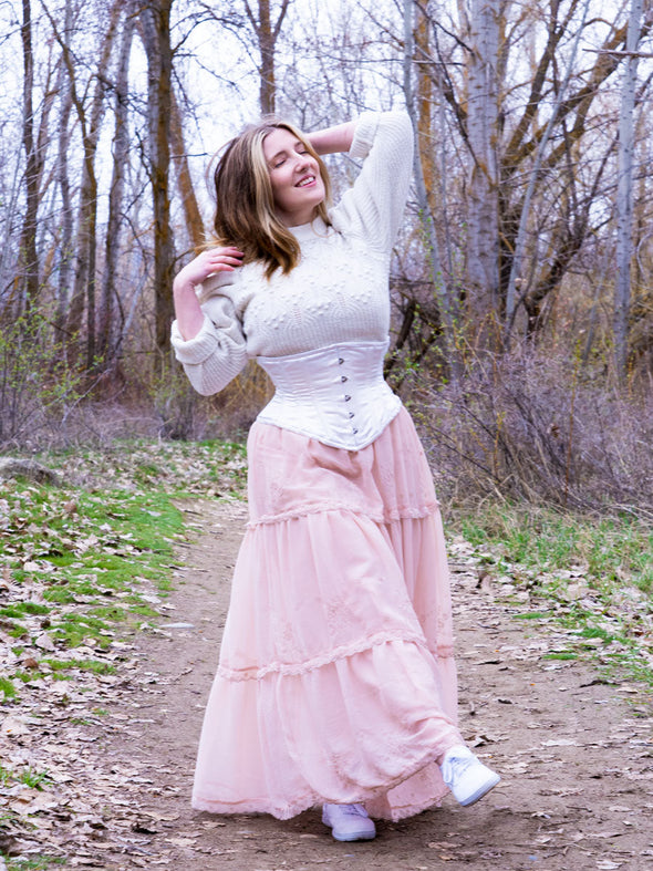 Model dressed in an ivory sweater and corset over a pink maxi skirt