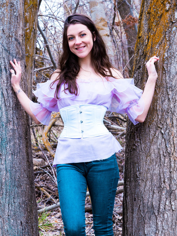 cute smiling model wearing a periwinkle ruffled blouse with jeans and a corset to complete the outfit