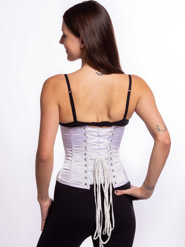 Back lace up detail of a Cute athletic build model wearing a modern curve corset in white satin with black leggings and black bra