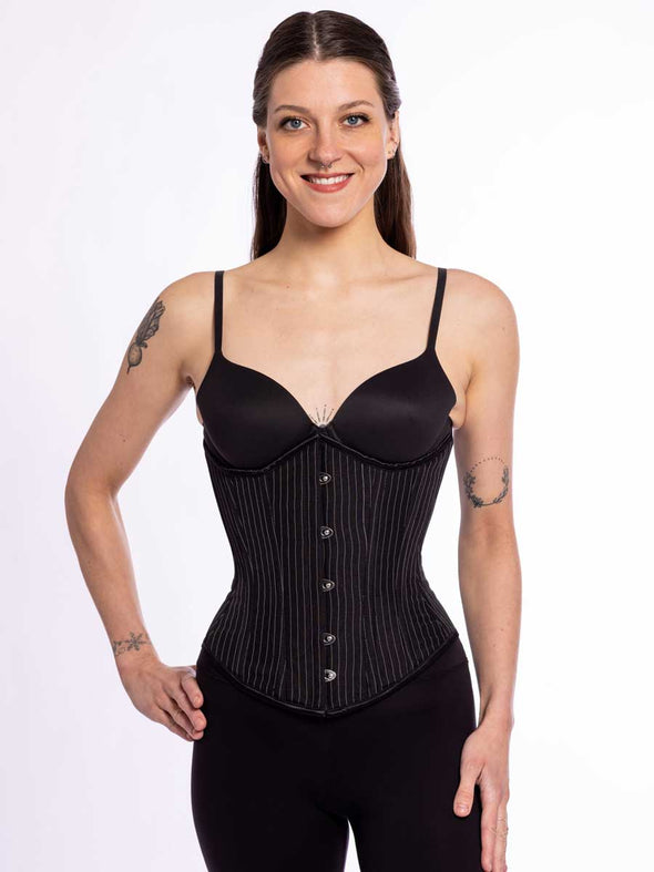 cute corset model wearing black leggings and black bra with a black pinstripe everyday corset that can be worn for fashion or waist training