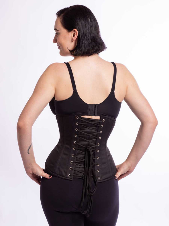 Female model wearing a cs411 long black cotton corset over leggings and a bra showing the back lace up view