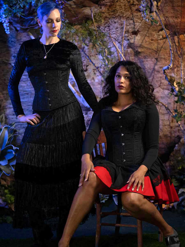 Two models one wearing the cs411 longline romantic curve black brocade over a velvet dress and the other in the cs 530 black brocade overbust corset top wearing a black shirt and red and black skirt