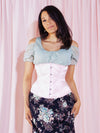 Smiling model wearing a floral skirt and gray cold shoulder top with a light pink everyday corset 