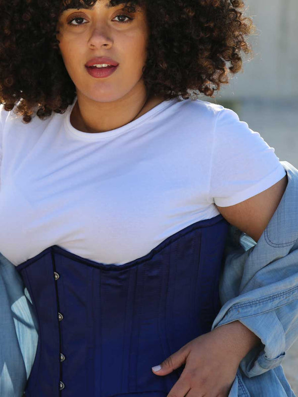 Close up of a model wearing the cs426 standard satin corset in navy with a white tshirt and chambray overshirt