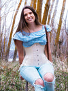 Model wearing a ruffled blouse and ripped jeans with boots wearing a longline ivory corset with hip ties to complete her outfit