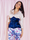 Model wearing floral pants and a metallic shirt with a navy hourglass corset to complete her outfit