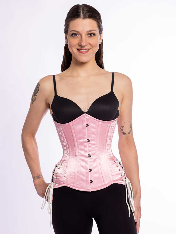 smiling cute corset model wearing an hourglass curve pink satin corset with hip ties over a black bra and leggings