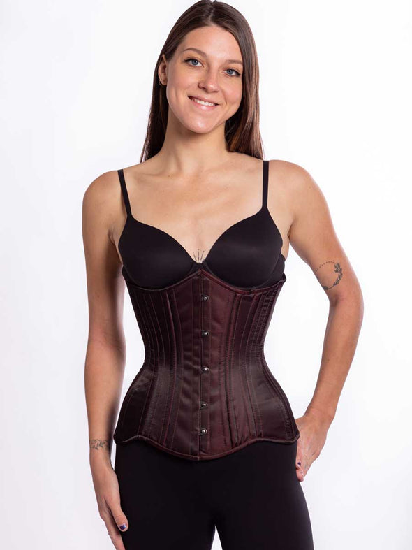 Female model wearing a curvy longline matte maroon satin corset over black leggings and a black bra