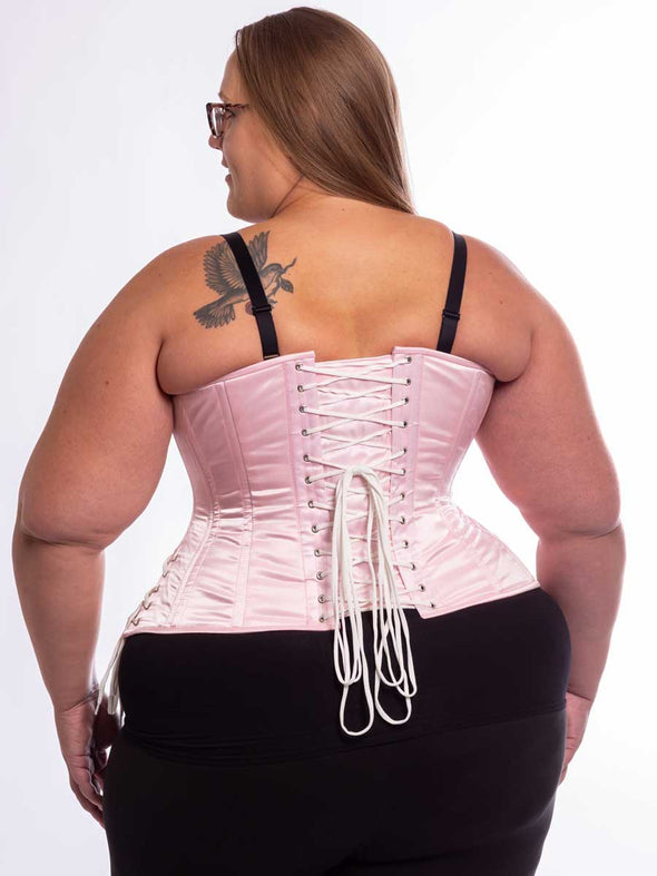 Curvy plus size model wearing the cs426 hourglass curve corset in light pink with hip ties showing the back lace up detail