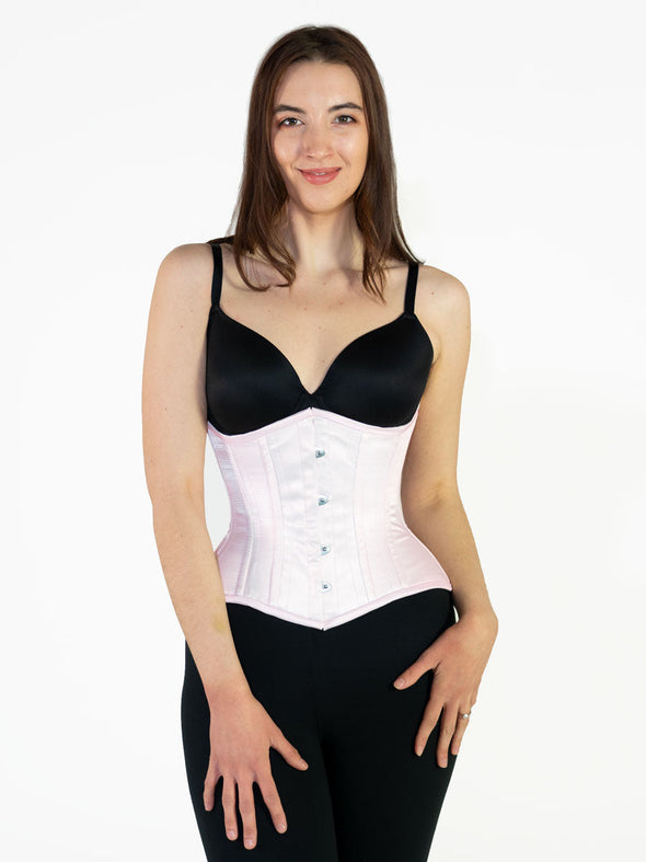 Model wearing black leggings and bra showing a light pink cosret over the outfit