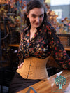 Model in a restaurant wearing the cs426 hourglass curve corset in beige cotton over a black floral print shirt and black skirt