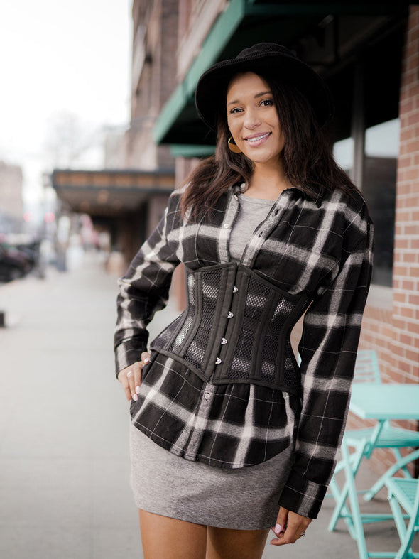 cute smiling model wearing a black and gray flannel shirt and gray tshirt dress with a black mesh corset to accessorize the outfit