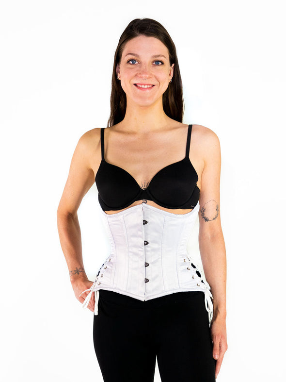smiling Model wearing our 426 with hip ties steel boned waist training corset in white satin over leggings and with a black bra