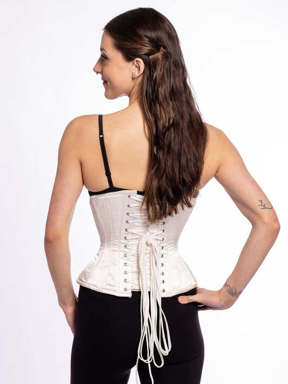 back lace up corset view of a cute corset model wearing an ivory satin everyday corset for waist training over a black bra and black leggings