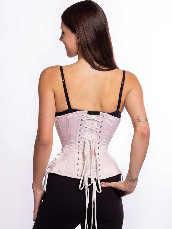 Back lace up detail of a Cute pink satin corset with hip ties worn by a female model wearing leggings and a bra
