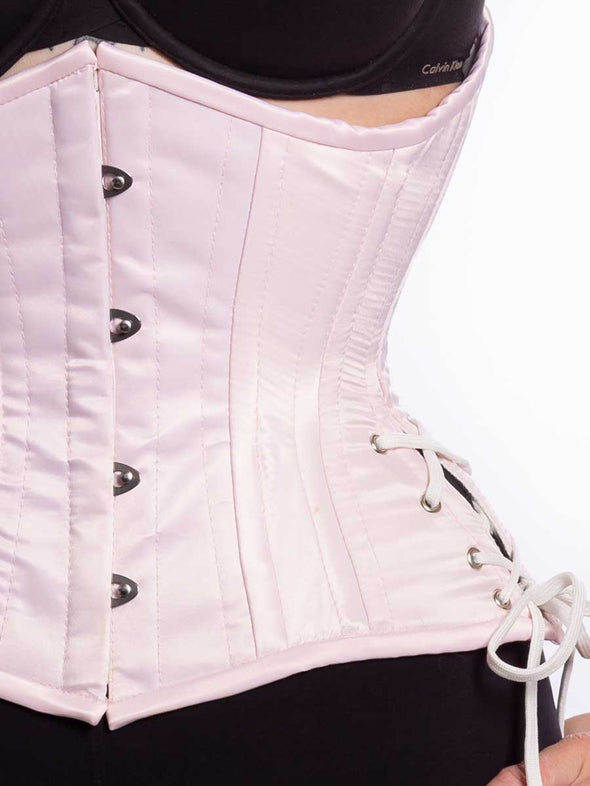 Front detail view of a Cute pink satin corset with hip ties worn by a female model wearing leggings and a bra