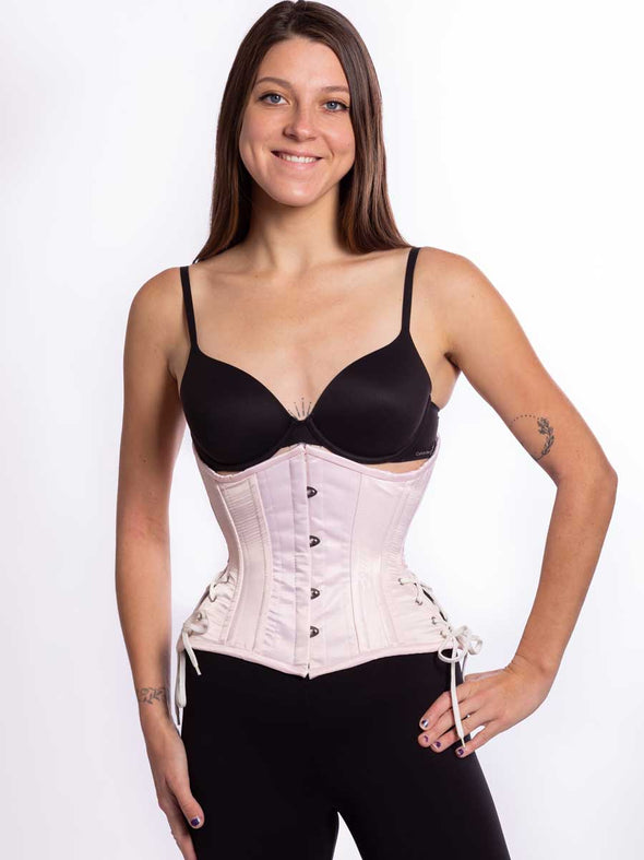 Cute pink satin corset with hip ties worn by a female model wearing leggings and a bra