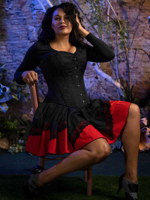 Seated model wearing the cs530 overbust corset top over a black shirt and red and black skirt