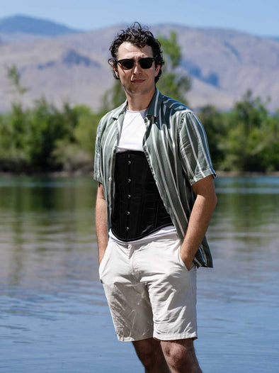 Male model standing in a river with sunglasses wearing the cs 701 corset in black satin