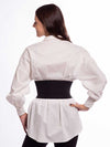 Model wearing a crisp white cotton tunic and a wide black leather corset belt over leggings