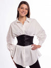 Model wearing a crisp white cotton tunic and a wide black leather corset belt over leggings