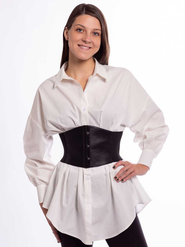 Model wearing a crisp white cotton tunic and a wide black leather corset belt over leggings